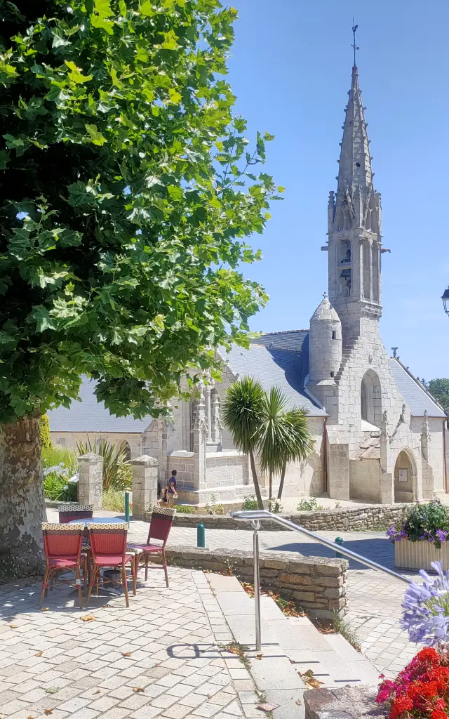 Vue de l'extérieur de l'église Notre Dame Izel avec la terrasse du bar Ty Butun et ses platanes