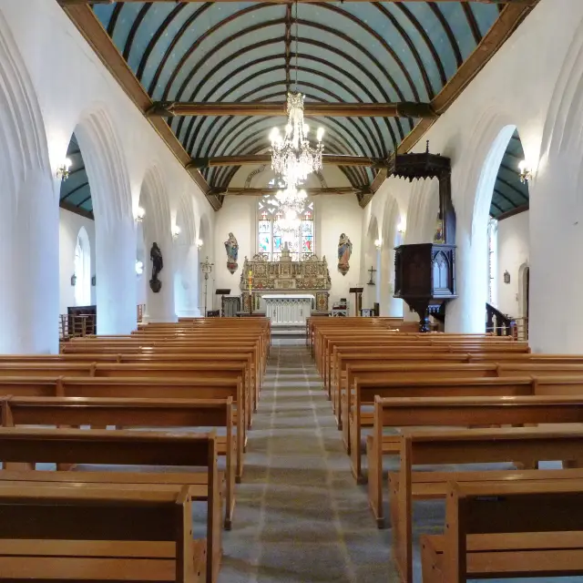 Das Innere der gotischen Kirche Notre Dame Izel Vor besteht aus dem Kirchenschiff mit Holzbänken, weißen Wänden und dem Altar mit einem Glasfenster im Hintergrund; und dem blauen Gewölbe mit gemalten Sternen.