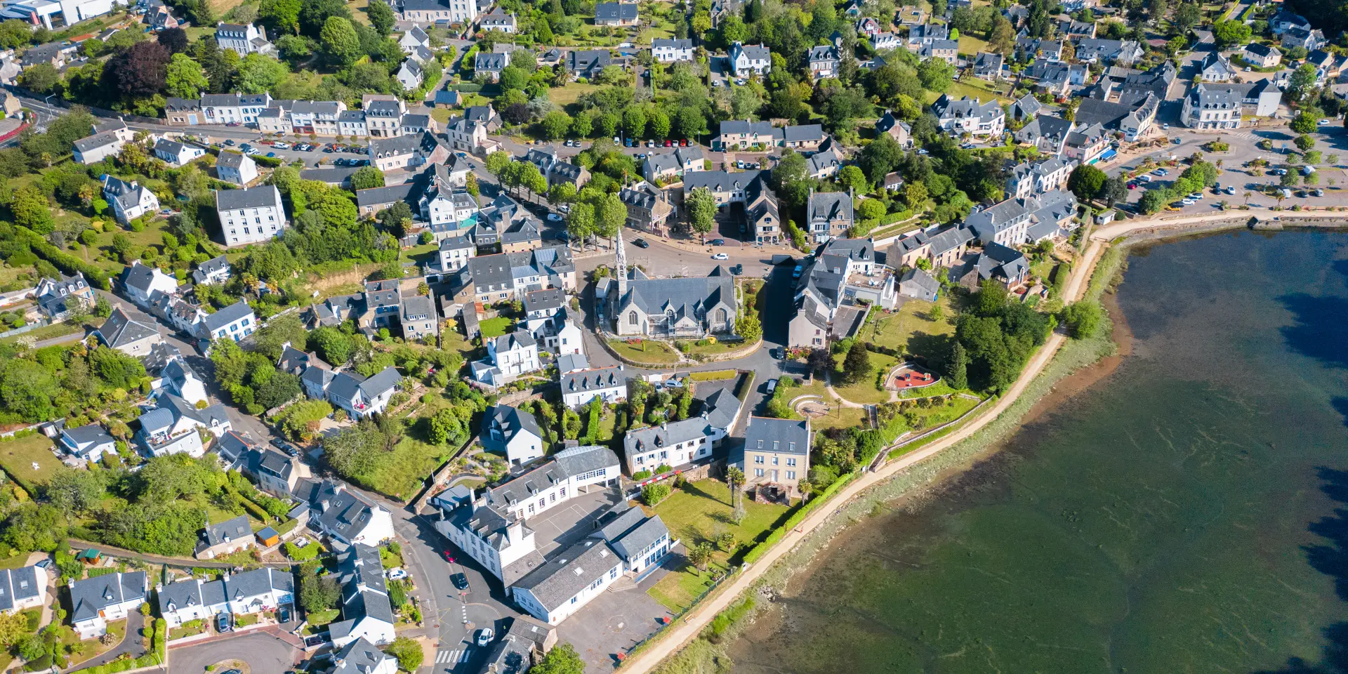 Luftaufnahme der Kirche Notre Dame Izel Vor und des Marktfleckens La Forêt mit Häusern und einem Teil der Bucht von La Forêt