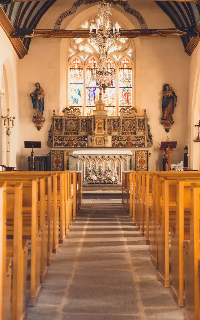 Het interieur van de kerk Notre Dame Izel Vor, met kerkbanken, hoogaltaar, beelden, centraal glas-in-loodraam en blauw sterrengewelf.