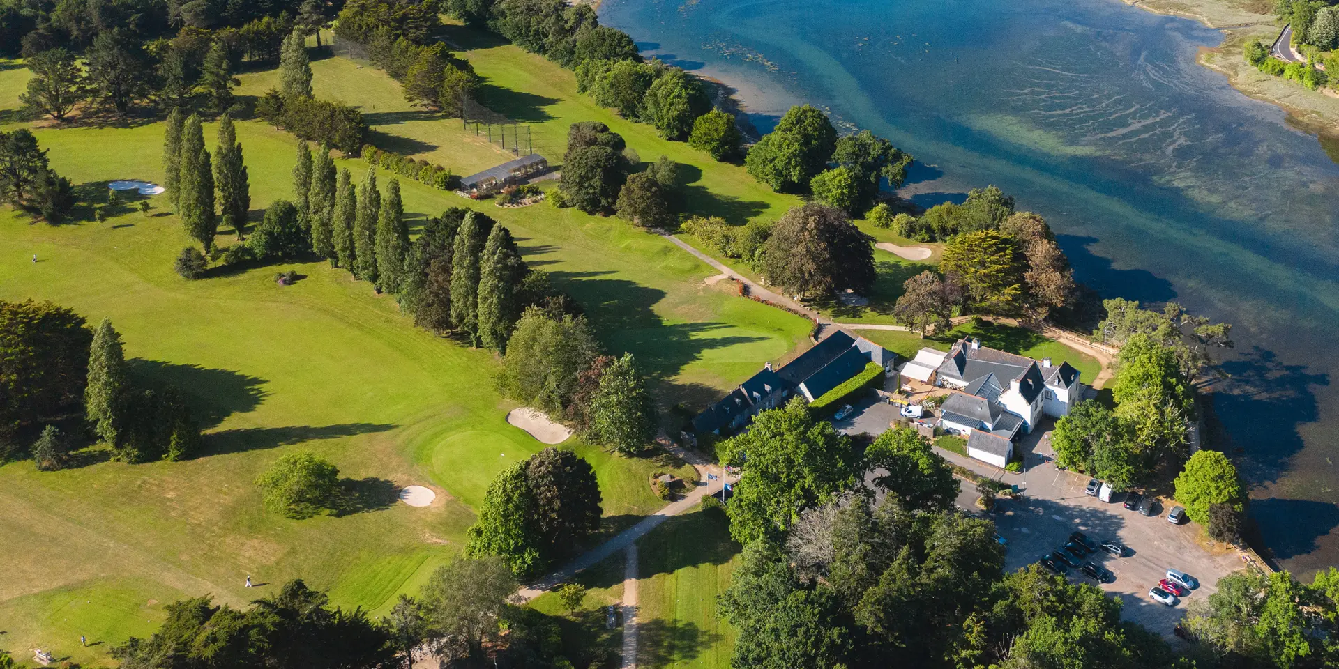 Foto, das eine Küste mit einer breiten Bucht/Mündung zeigt, einen Hafen mit vielen Booten auf der linken Seite, grüne Golfplätze im Vordergrund und Wohnhäuser auf der rechten Seite, dann das Meer im Hintergrund.