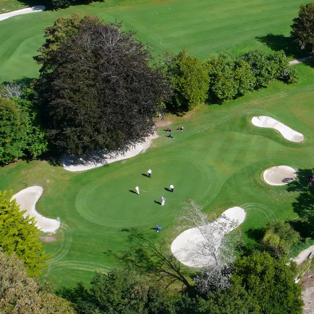 Aerial photo of a golf course (green lawns, several white sand bunkers, trees, a lake in the bottom right).