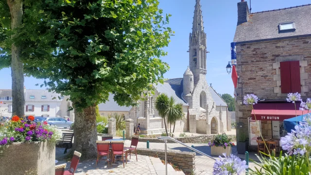 Vue de l'extérieur de l'église Notre Dame Izel avec la terrasse du bar Ty Butun et ses platanes