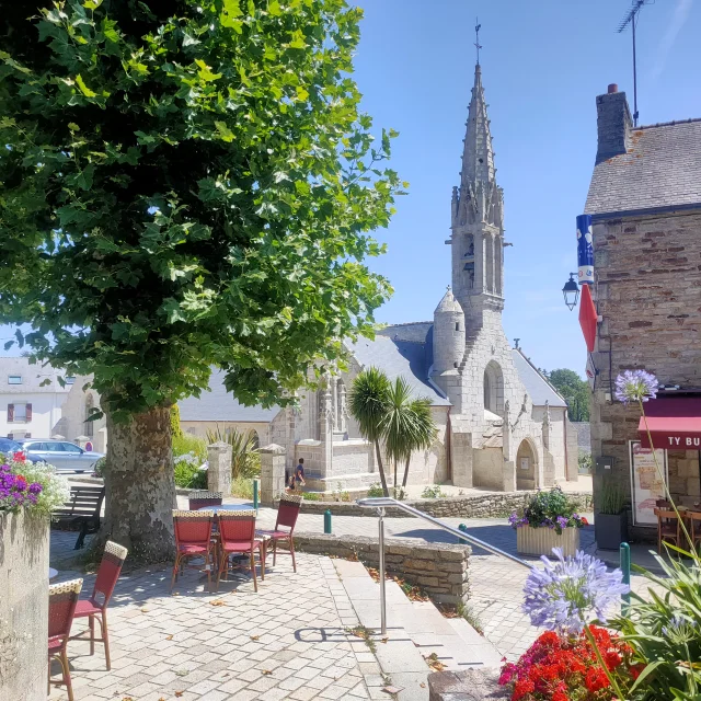 Vue de l'extérieur de l'église Notre Dame Izel avec la terrasse du bar Ty Butun et ses platanes