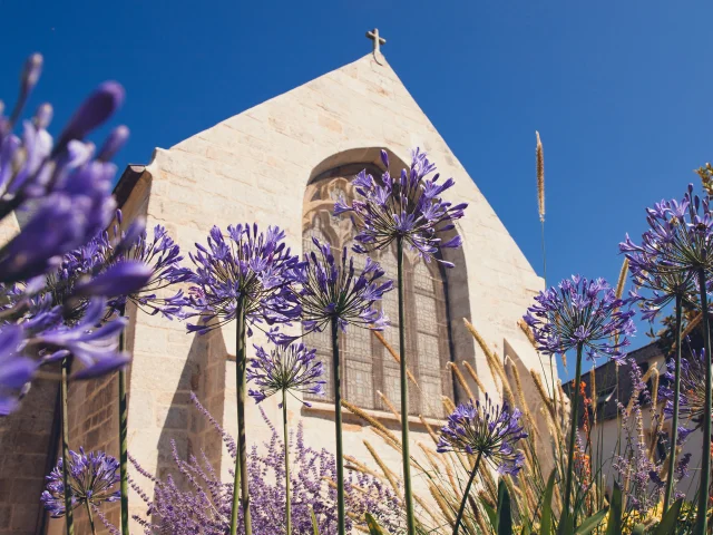 Vue extérieure de l'église Notre Dame Izel Vor avec des vitraux et des agapanthes mauves