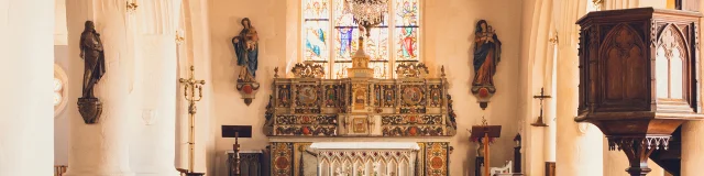 L'intérieur de l'église Notre Dame Izel Vor avec les bancs, le maitre autel, des statues, le vitrail central et la voute bleue étoilée.