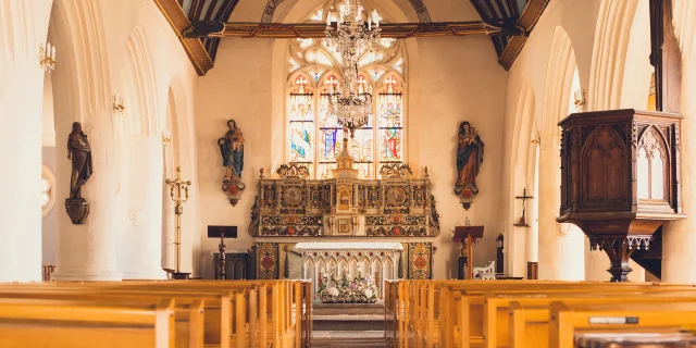 The interior of Notre Dame Izel Vor church, with pews, high altar, statues, central stained glass window and blue starry vault.
