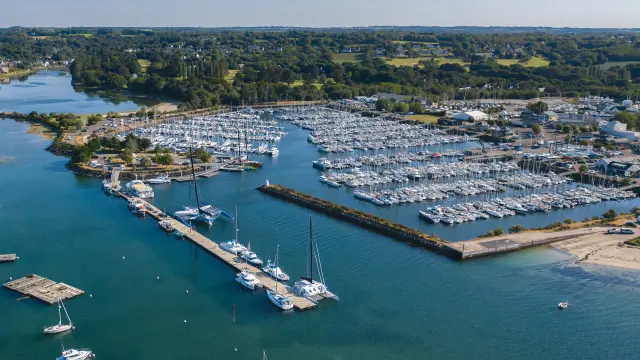 An aerial photograph showing a marina with rows and rows of moored boats, pontoons, a breakwater and a stretch of blue-green water; houses and green areas can be seen in the distance.