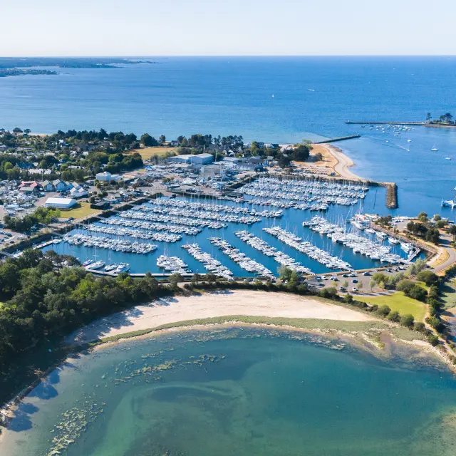 Luchtfoto van een jachthaven aan zee. De foto toont een jachthaven vol boten, pontons, een golfbreker en stranden/stranden met turquoise water en een groen gebied met bomen op de voorgrond.