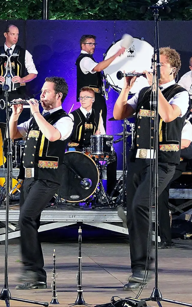 Une grande photo montre un groupe de musiciens sur scène (tenues noires et blanches), avec plusieurs instruments (cornemuses, percussions, cuivres), des micros sur pieds au premier plan et des éclairages de scène (violet, jaune/orange). Des fûts noirs servant de décor portent des logos blancs (dont un crâne) et un autre fût affiche “Hénaff”.