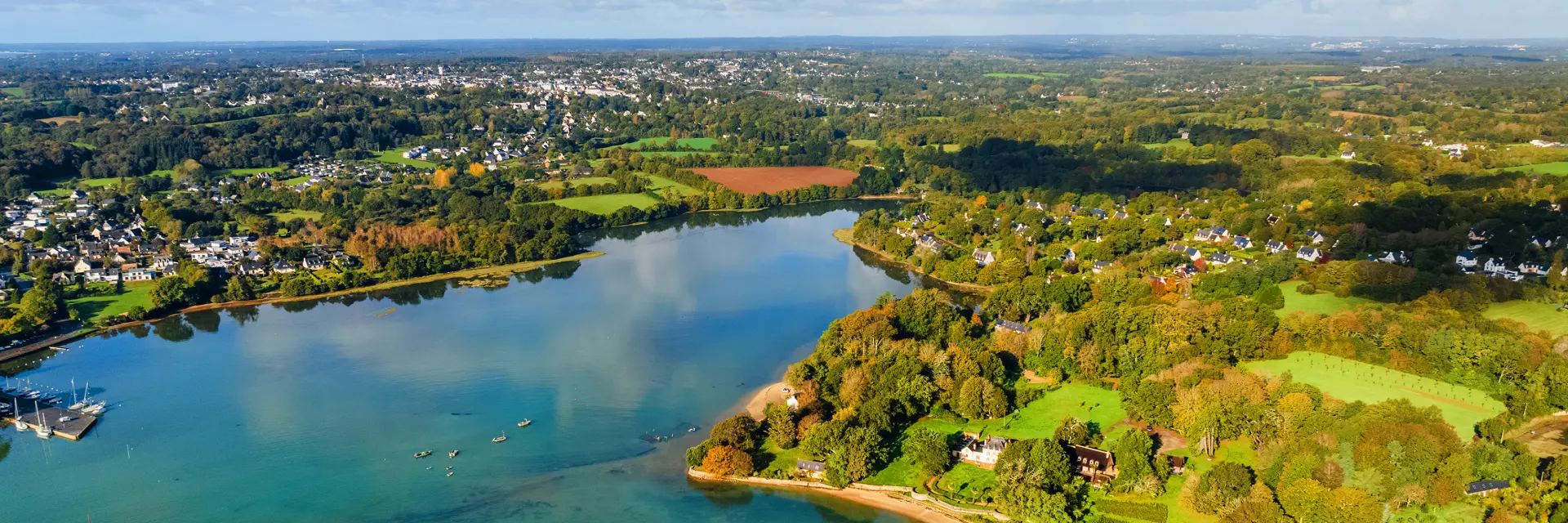 a large aerial photo of a green cove/coast and blue-green water, under a blue sky with large clouds.