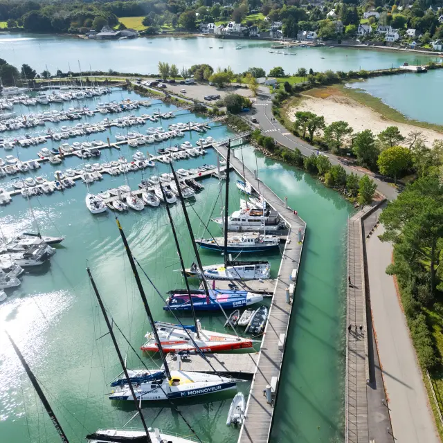 an aerial photograph in the centre left. The photo shows a marina full of boats on the left, a dyke/road in the middle, a wooded area on the right, and a large body of water on the right with a curved beach; in the background, houses and vegetation under a cloudy sky.