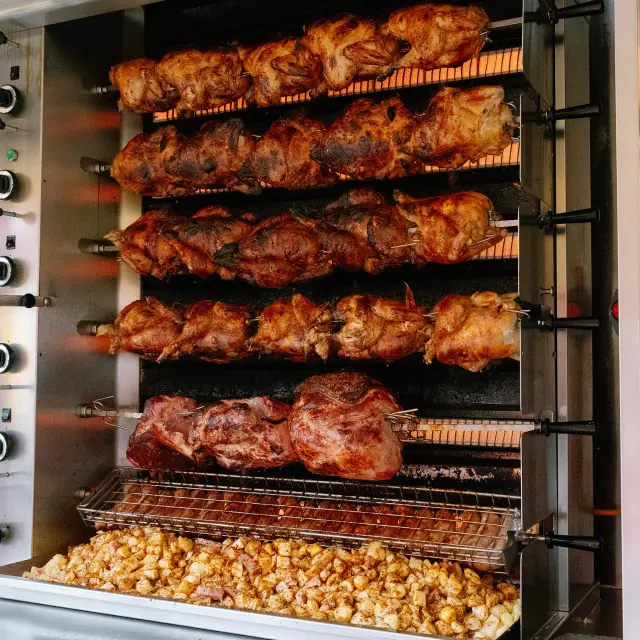 Une photo de rôtisserie : plusieurs poulets rôtis alignés sur des broches dans un four/gril, et des pommes de terre en bas