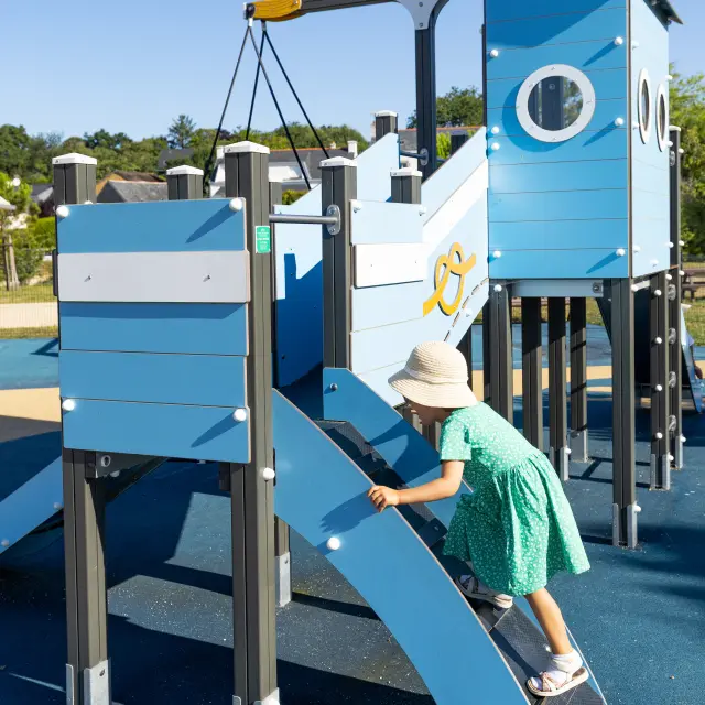 Une photo de jeux pour enfants : une structure bleue type bateau avec un enfant qui monte dessus