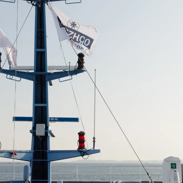 Une photo d’un mât de navire bleu avec des feux et un drapeau blanc “BreizhGo”, sur fond de ciel et mer.