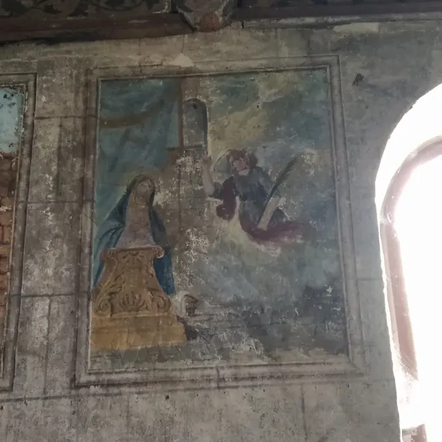 Foto eines alten Wandgemäldes. Die Hauptszene zeigt eine blau verschleierte Frau (Maria) vor einem hölzernen Pult und rechts einen Engel (Gabriel) im Flug, rotes Gewand, mit einem sichtbaren Flügel. Auf der linken Seite ist eine weitere Teilszene eingerahmt, aber abgeschnitten. Ein großer, heller Fensterbogen erscheint überbelichtet auf der rechten Seite des Bildes. Das Fresko ist in Blau-, Grau- und Brauntönen gehalten und weist Gebrauchsspuren und Risse auf.