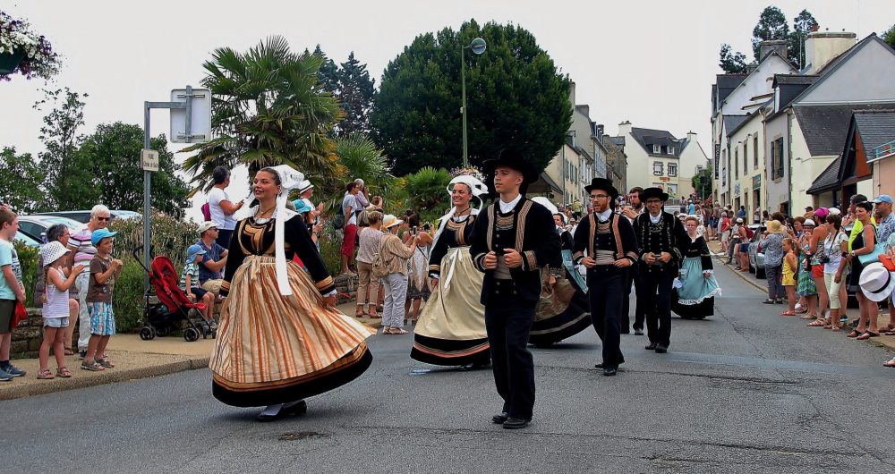 Personnes en costume traditionnel breton qui dansent en défilant dans la rue principale de La Forêt-Fouesnant